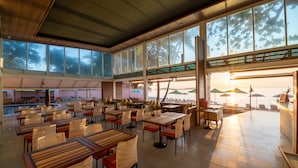 A spacious indoor dining area with multiple tables and chairs, large windows, and a view of the pool and beach. - Baan Samui Resort (Koh Samui)