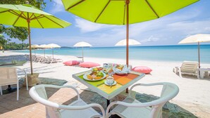 A beachside dining area with tables and chairs under umbrellas, overlooking the sea. - Baan Samui Resort (Koh Samui)