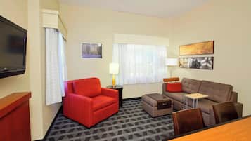 A hotel room with a red armchair, a brown sofa, a small table, a TV, and a window with curtains.