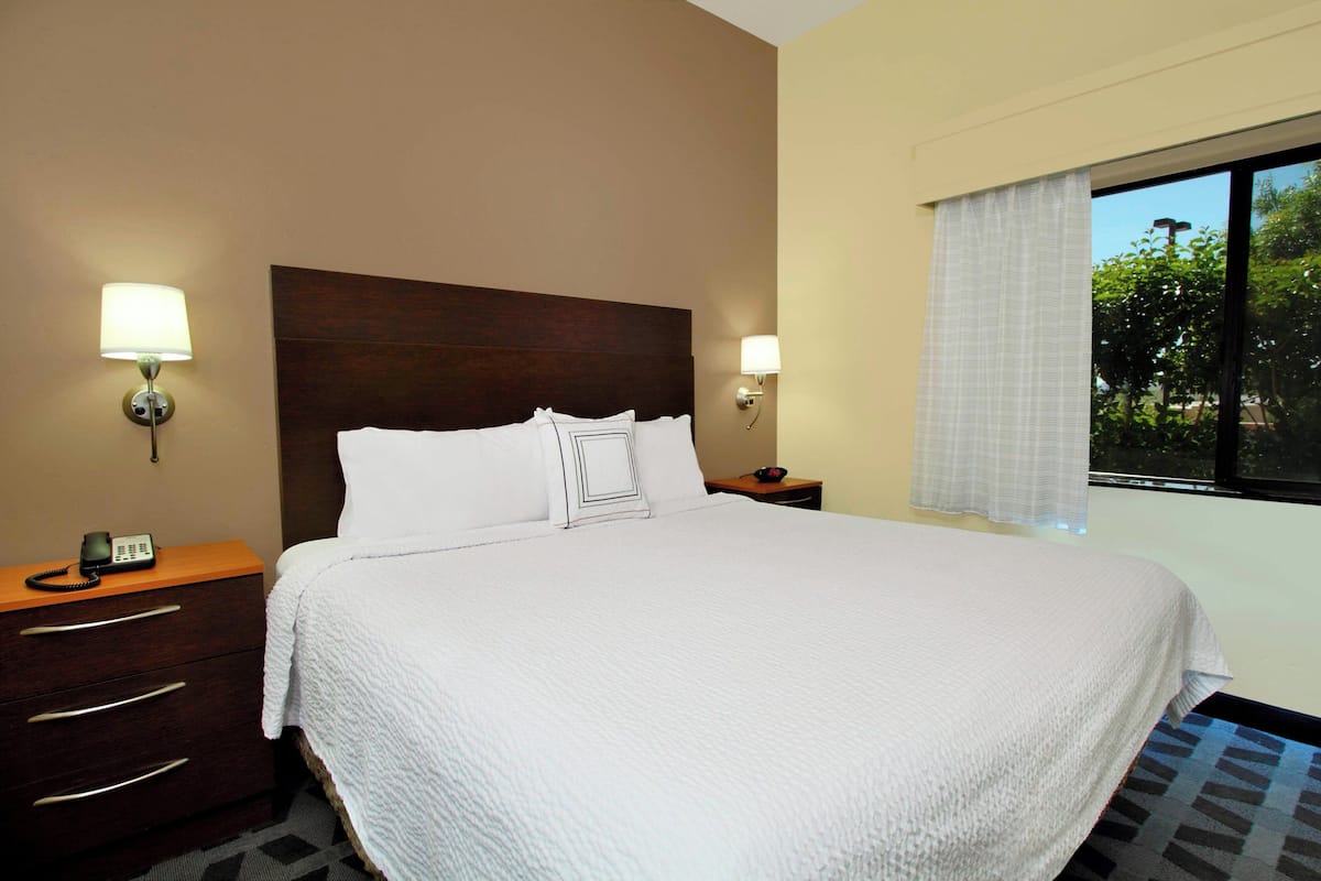 A hotel room with a large bed, two bedside tables with lamps, a wooden nightstand, and a window with curtains.