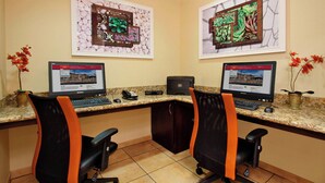 A workspace with two desks, each with a computer, keyboard, and mouse. There are two chairs with orange accents, and a small cabinet between the desks.