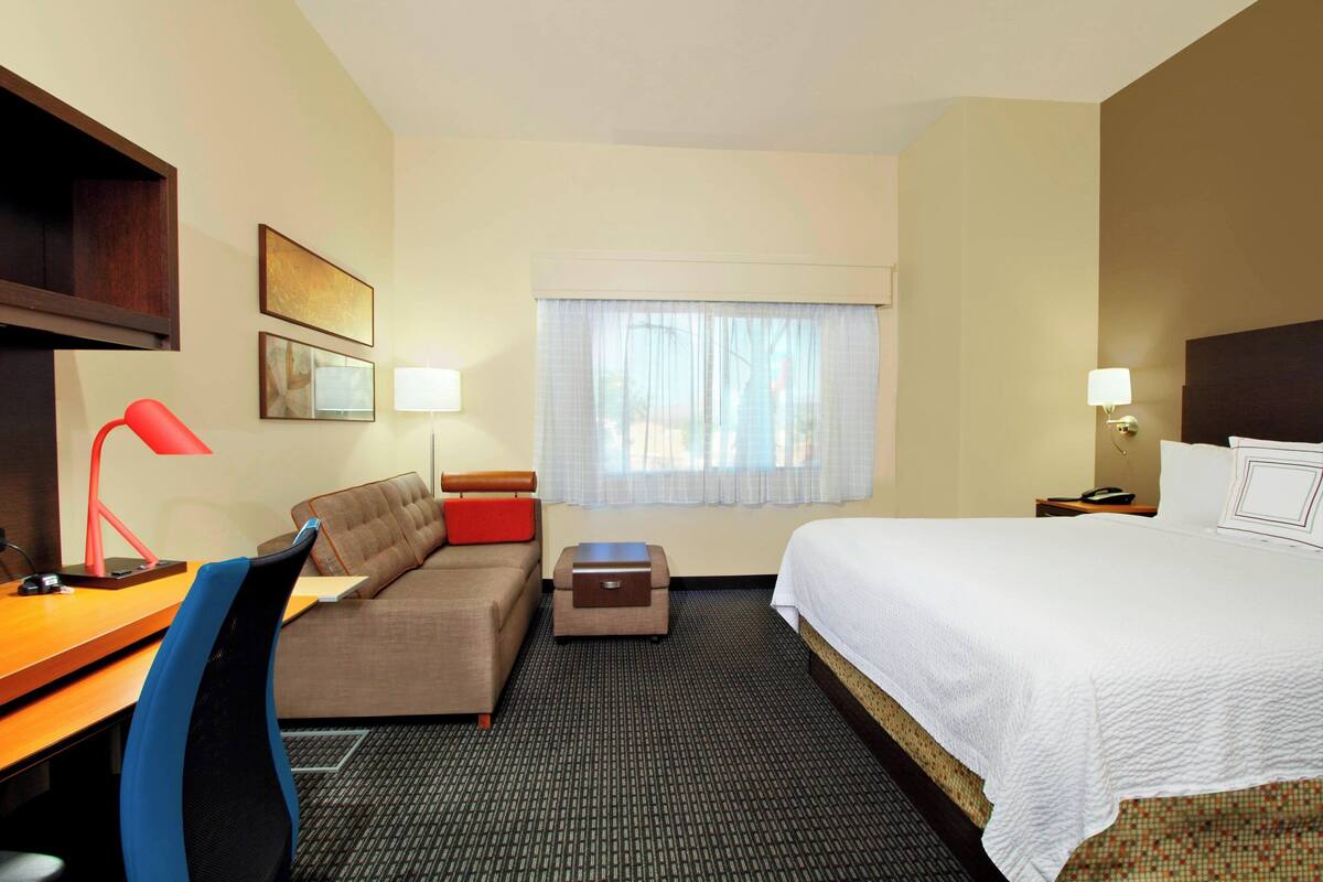 A hotel room with a bed, a desk, a chair, a sofa, a small table, and a window with curtains.