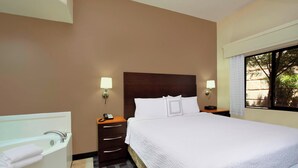 A hotel room with a large bed, a separate bathroom with a bathtub, and a window providing a view of trees.