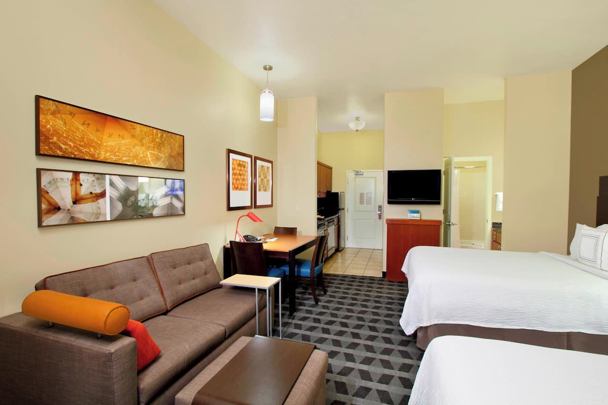 A hotel room with a sofa, a small table, a bed, a TV, and a kitchen area.