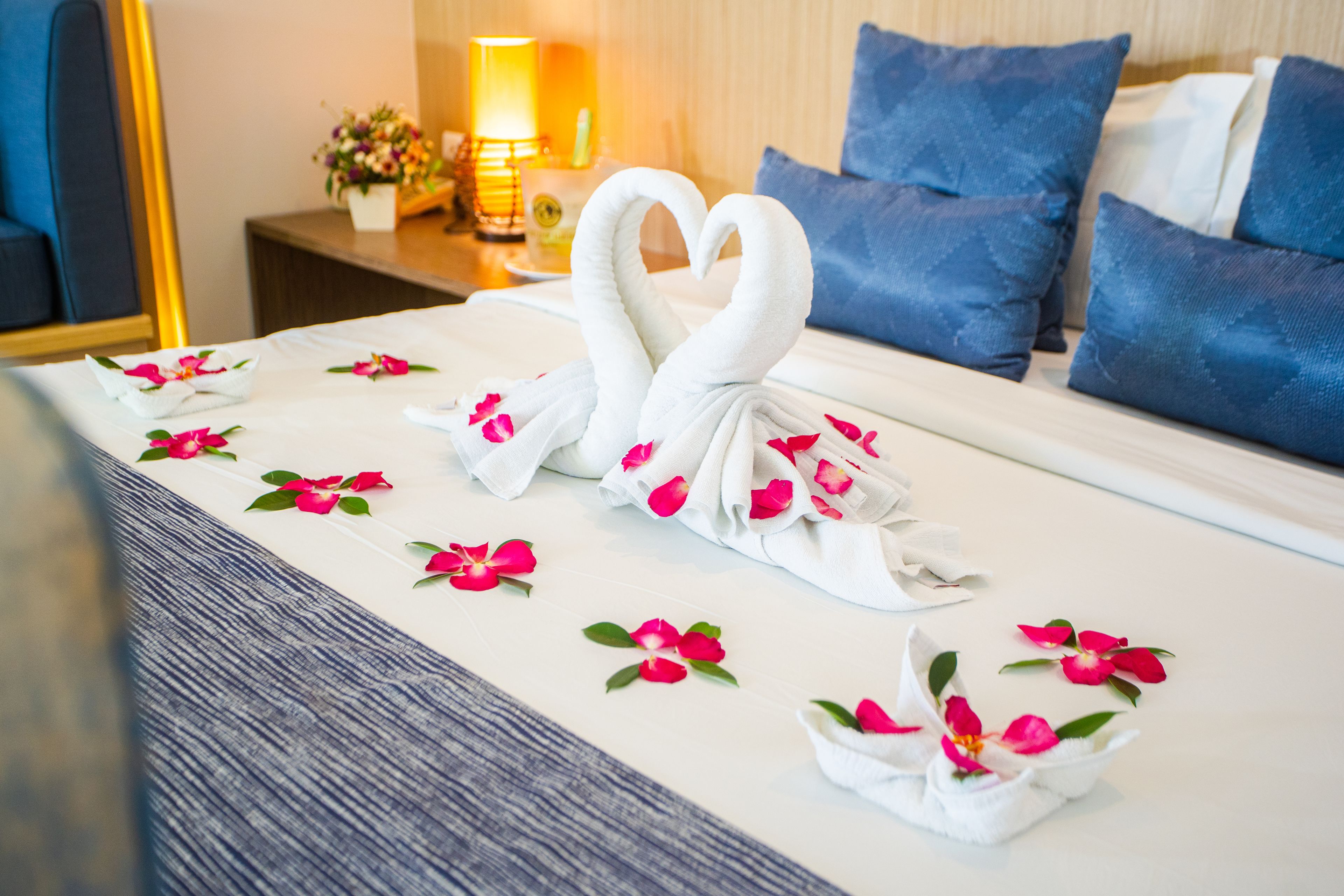 A neatly made bed with two swan-shaped towels and pink flower petals arranged on the bedspread.