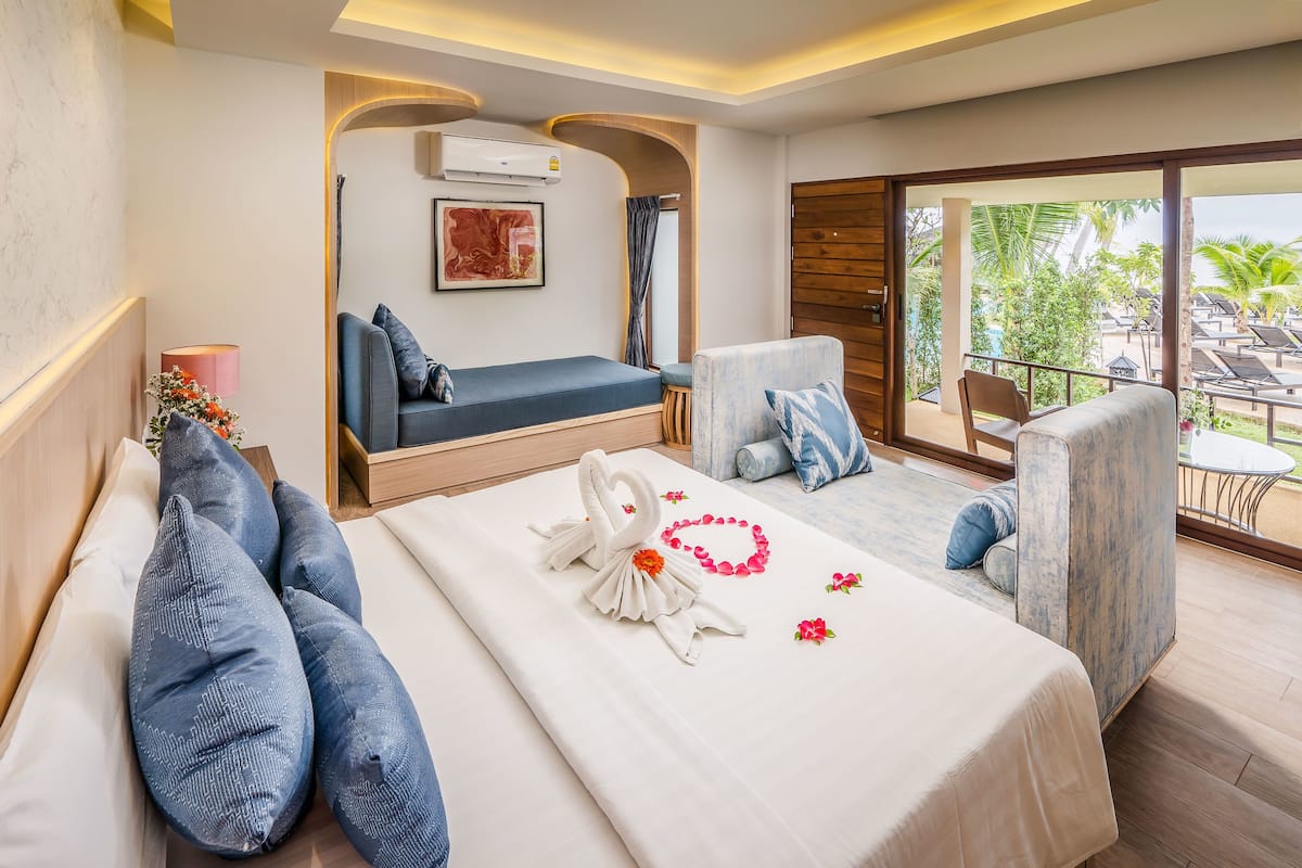A hotel room with a bed, a sofa, and a balcony with a view of palm trees.
