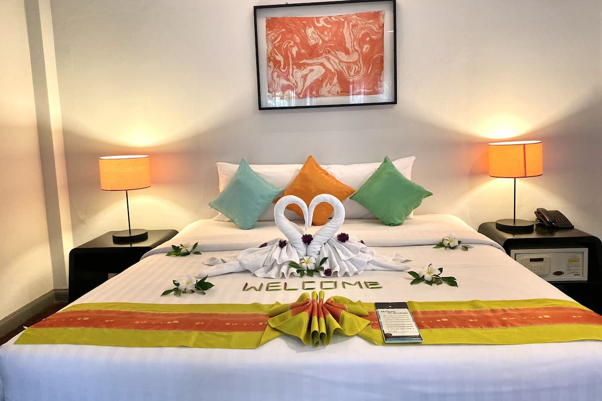 A hotel room with a neatly made bed, a welcome mat, a framed artwork on the wall, and two bedside lamps.