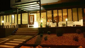 Entrada de hotel con galería techada, zona de bufé y mesas al aire libre.