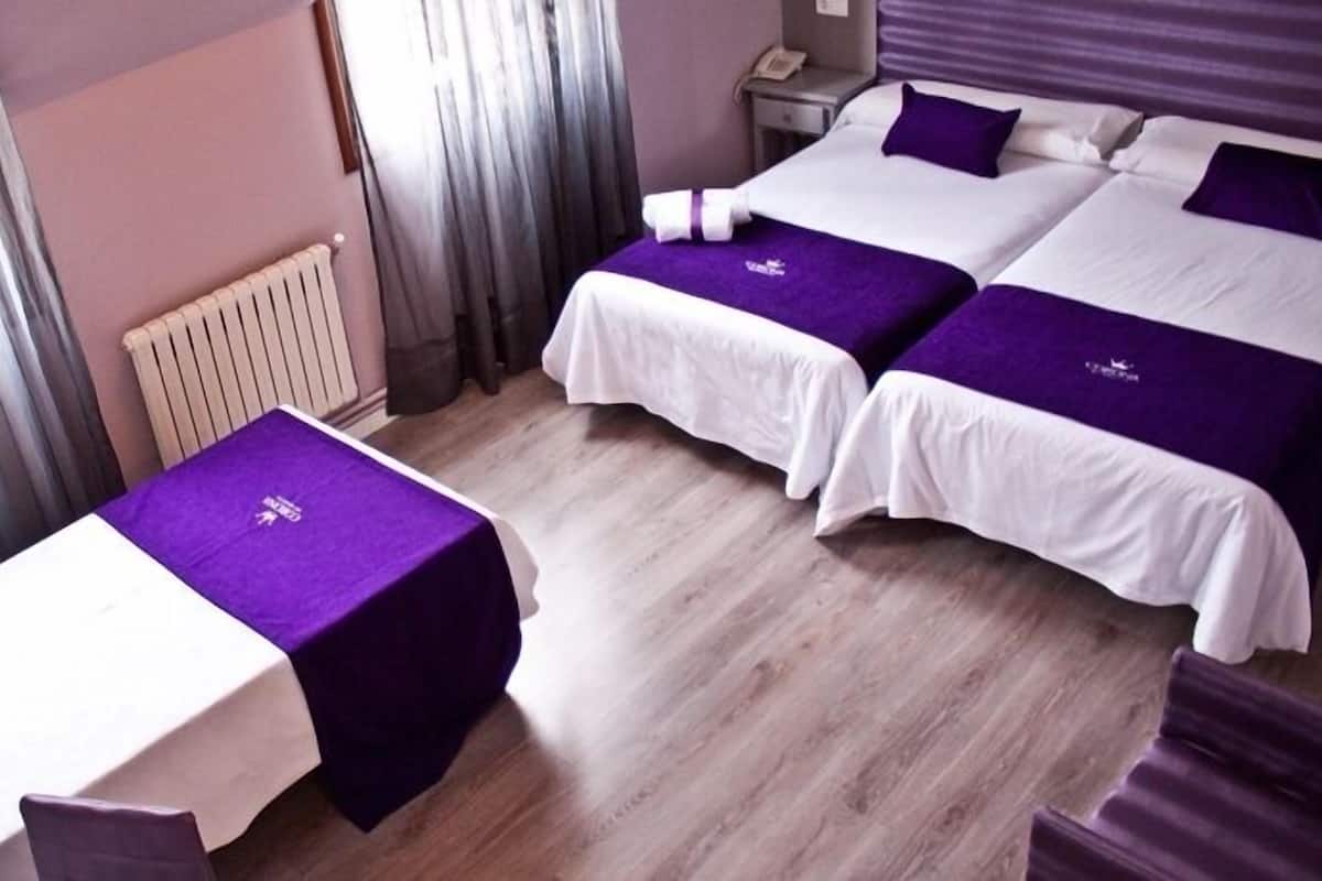A hotel room with two beds, a small table, and a radiator.