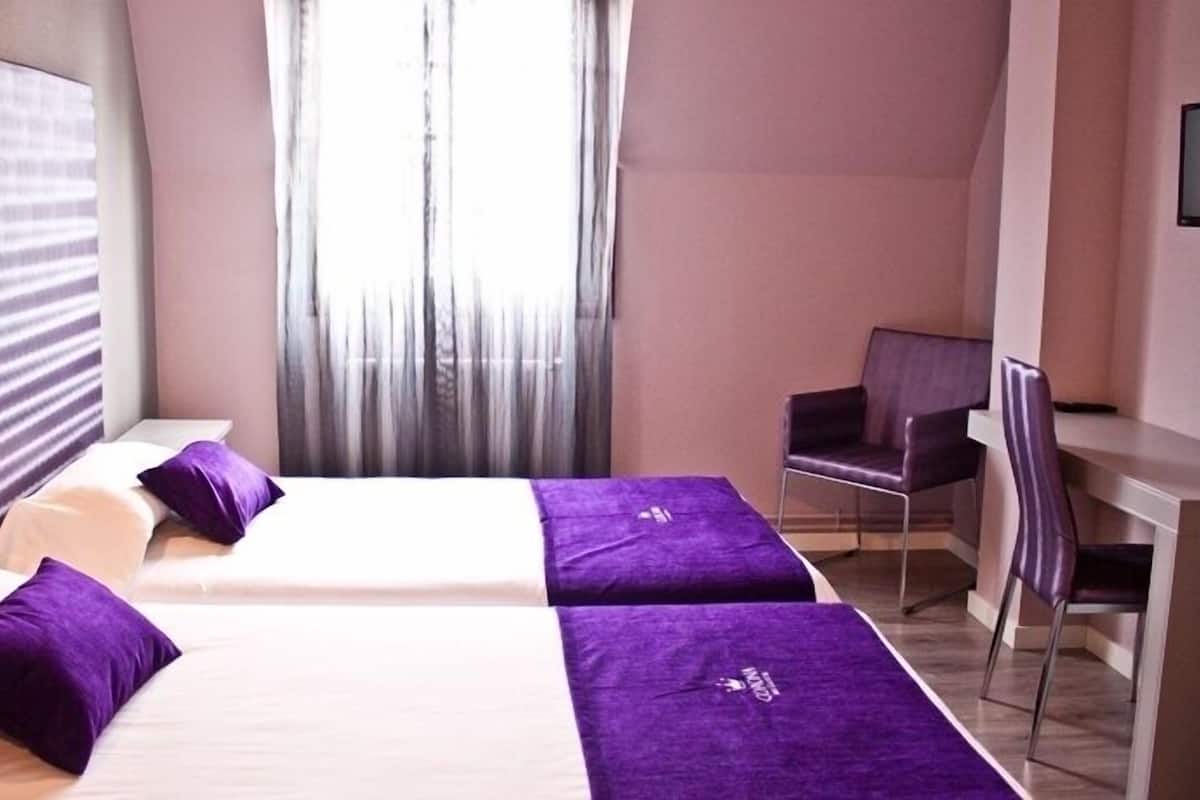 A hotel room with two beds, a desk, a chair, and a TV.