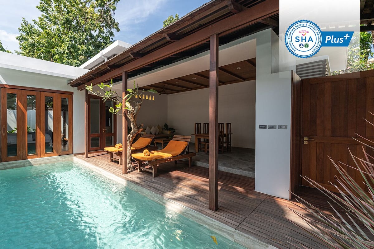 A swimming pool with wooden deck and lounge chairs, a covered seating area, and a wooden gate.