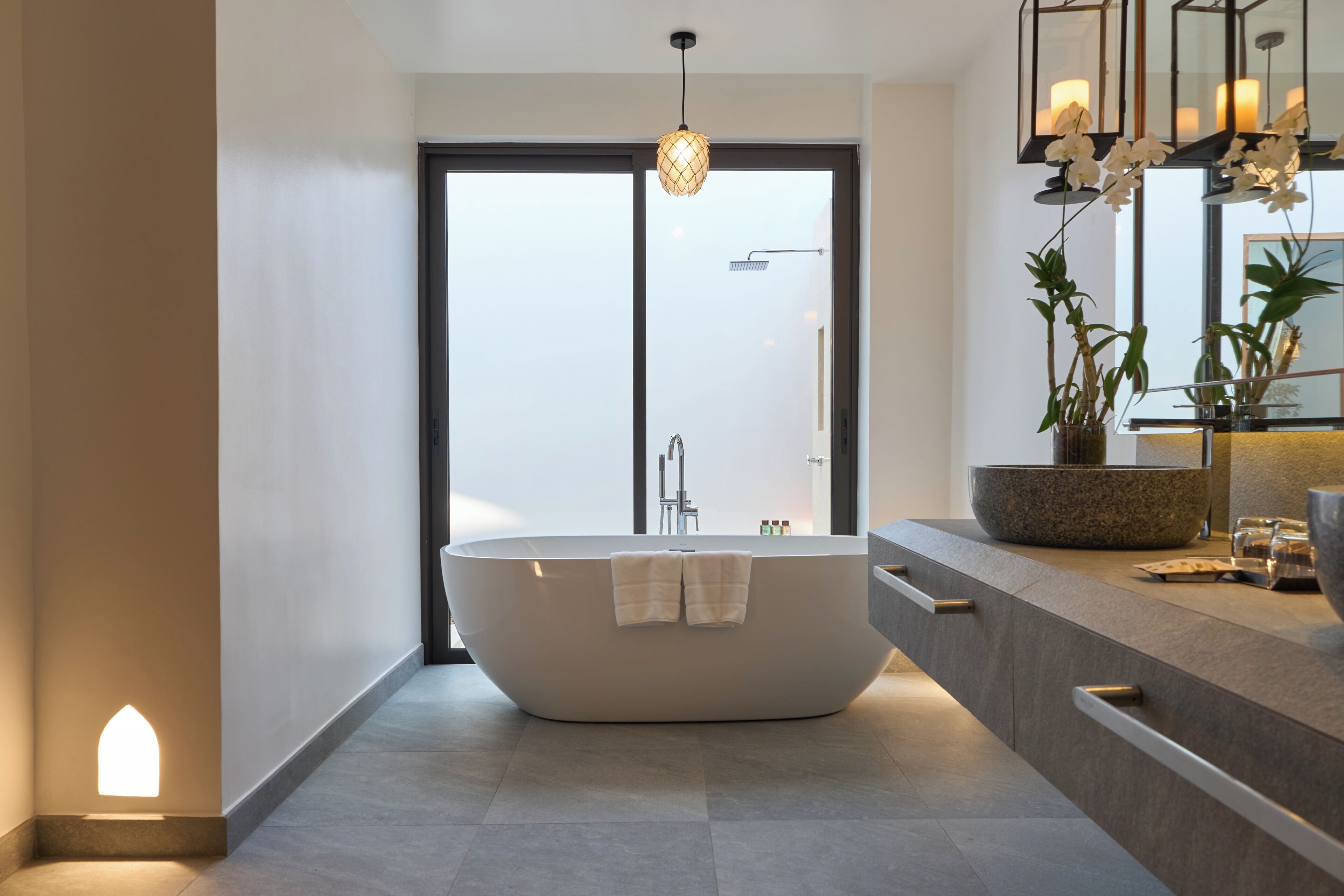 A modern bathroom with a freestanding bathtub, a large mirror, and a potted plant.