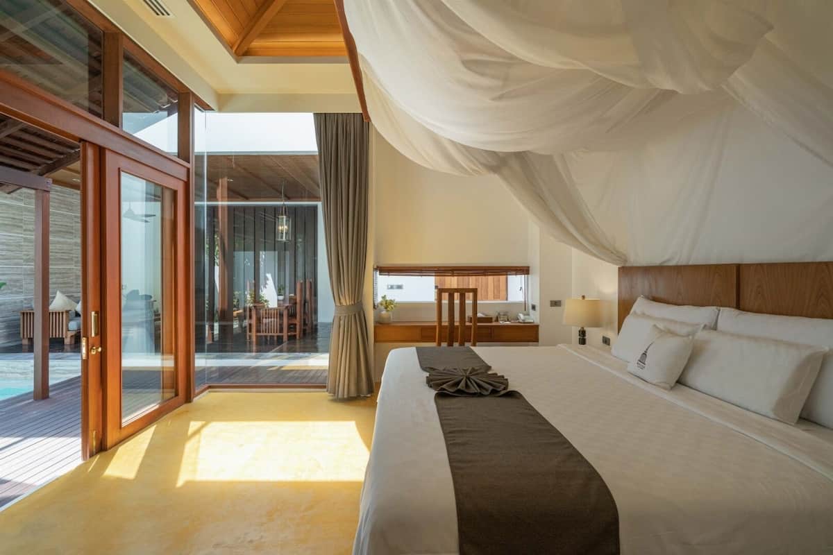 A spacious bedroom with a large bed, a desk, and a view of a pool.