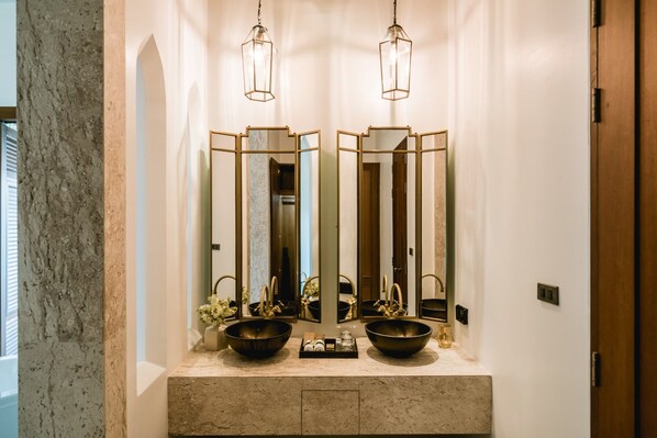 Un baño con dos lavamanos, cada uno con un lavabo grande y un espejo encima. Hay dos lámparas colgantes sobre los espejos.
