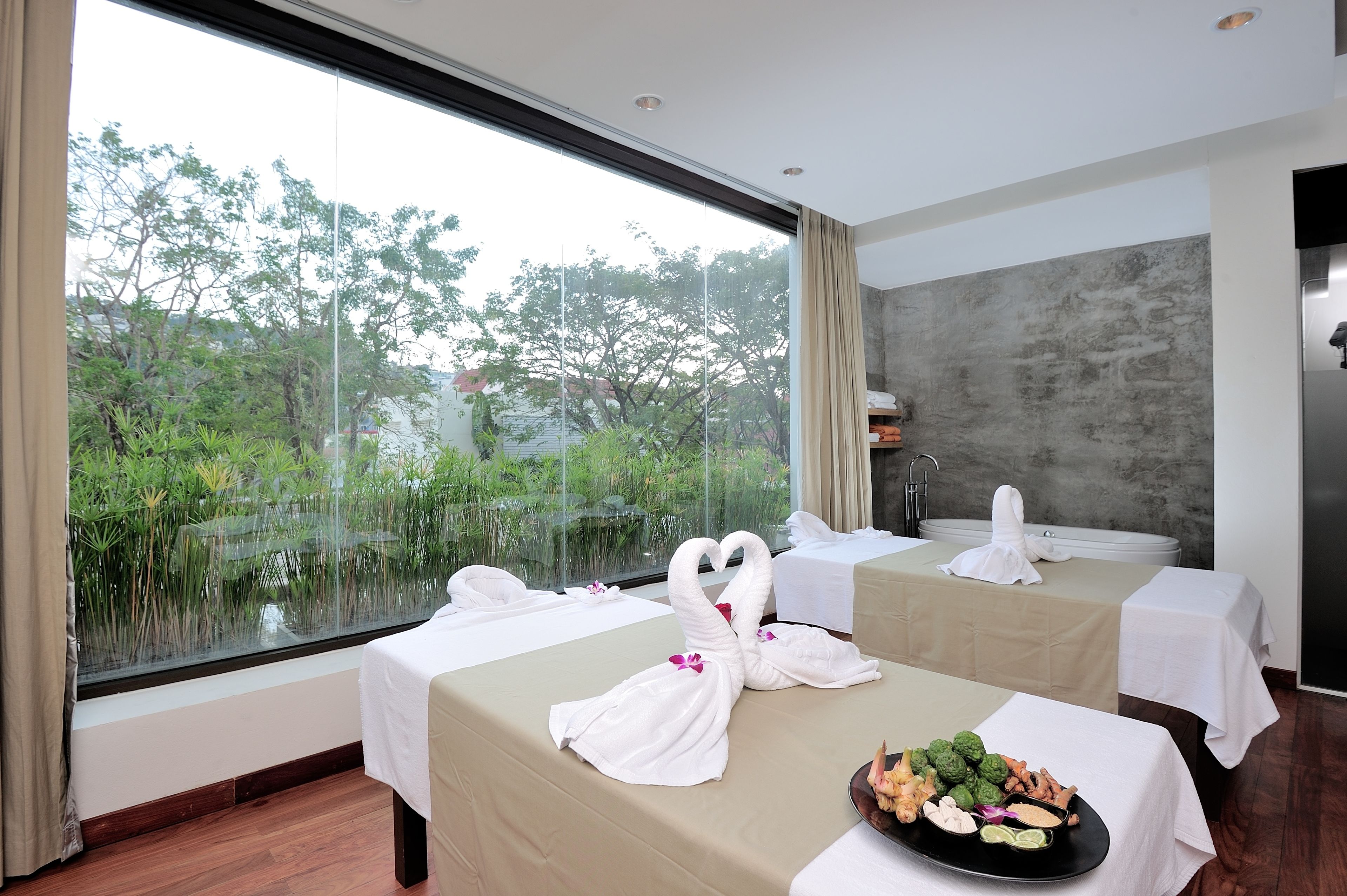 A hotel room with two beds, a large window with a view of greenery, and a table with a fruit platter.