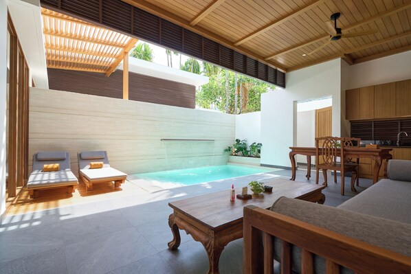 Uma área de piscina moderna ao ar livre, com espreguiçadeiras, uma mesa de madeira e um espaço com cozinha.