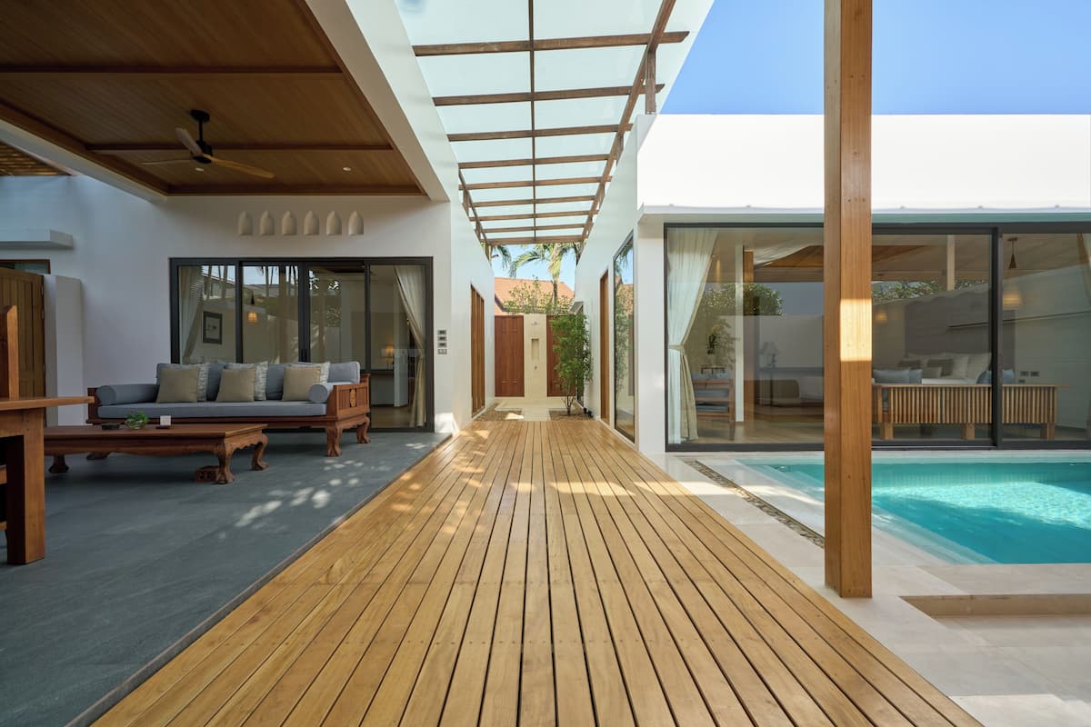 A modern outdoor living area with a wooden deck, a pool, and a covered seating area.