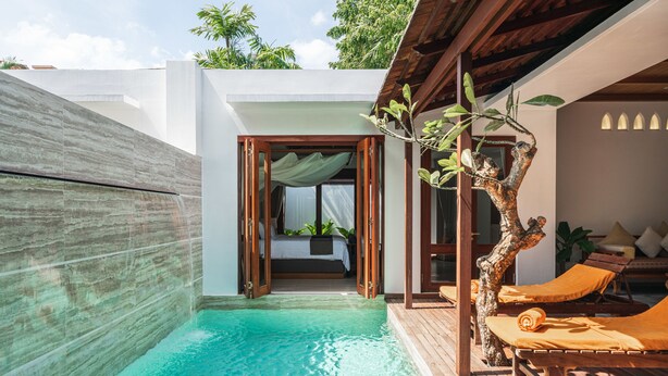 A private pool area with a wooden deck, a bed with a view of the pool, and a lounge area with sun loungers.