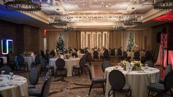 Un salón de banquetes con mesas redondas, sillas y árboles de Navidad.