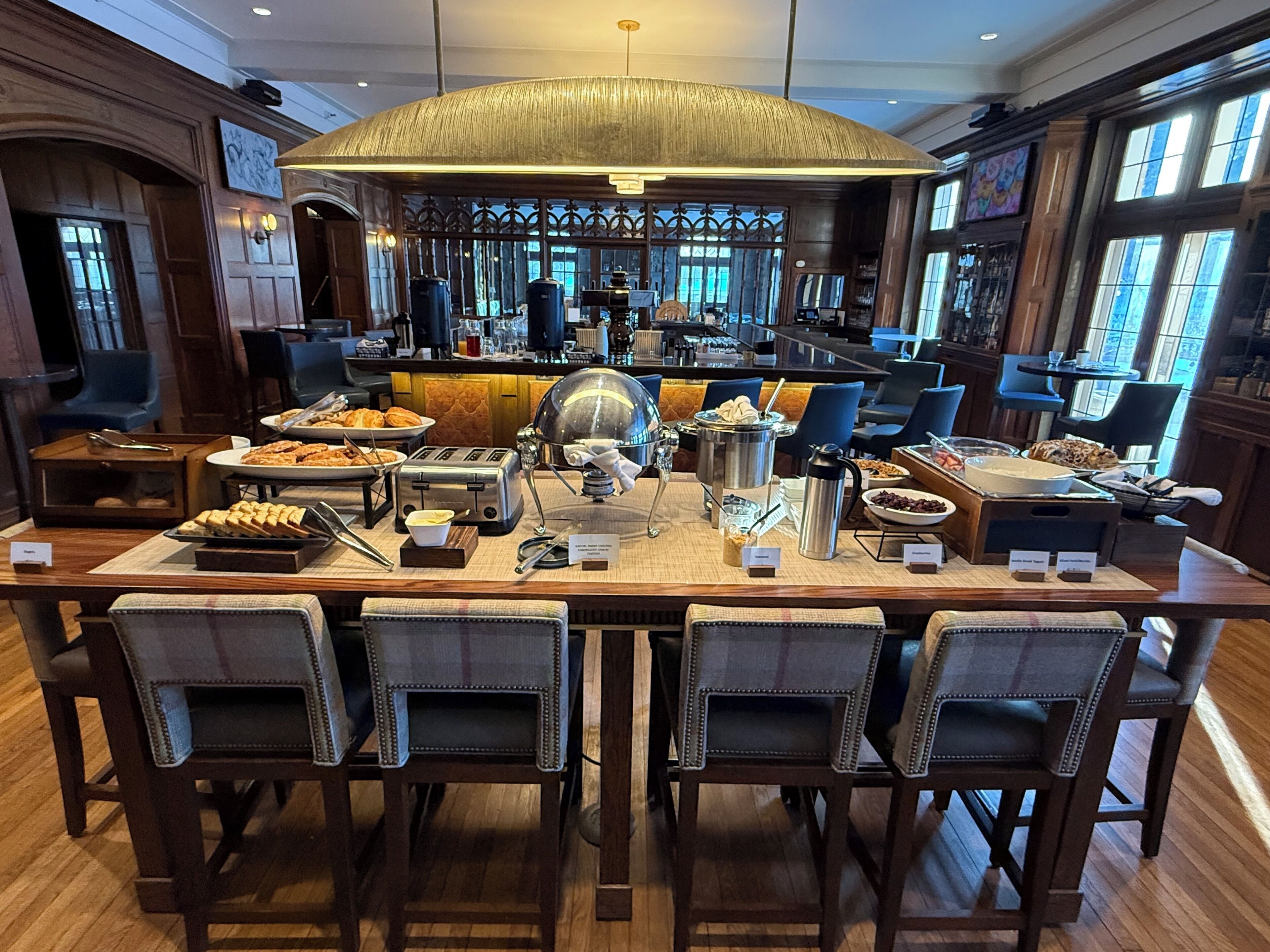 A breakfast buffet setup with various food items, a coffee machine, and seating arrangements.