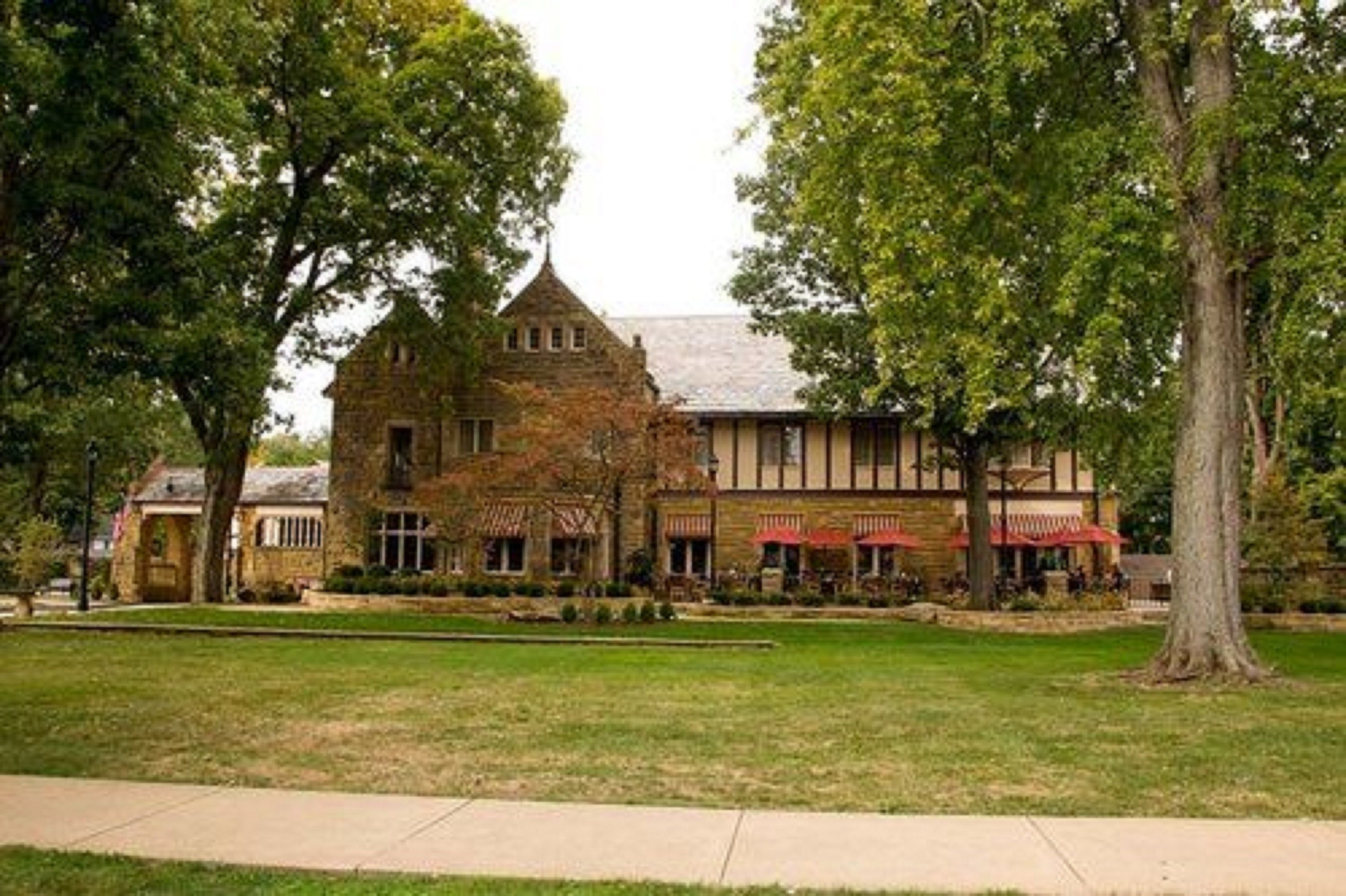 A historic stone building with a prominent tower, surrounded by lush trees and a well-maintained lawn.
