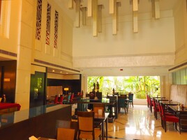 A spacious hotel lobby with a long reception desk, multiple seating areas, and a view of lush greenery outside.