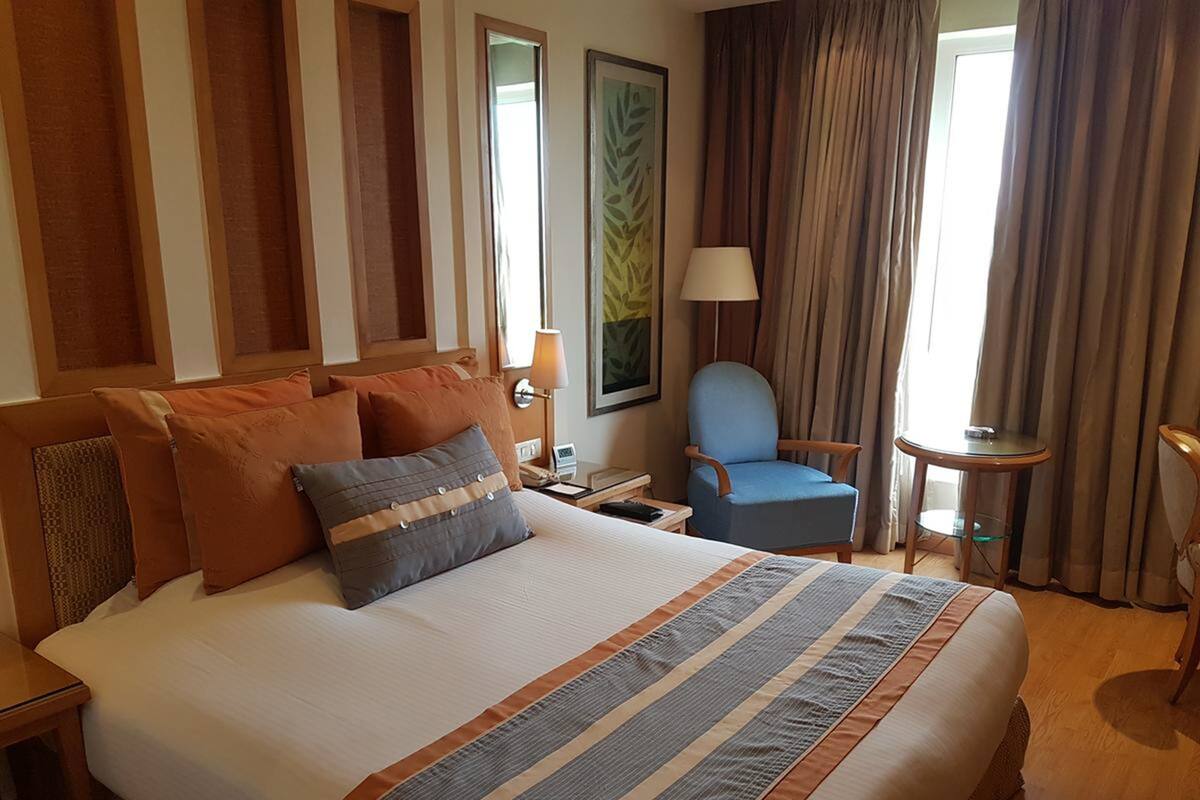 Habitación de hotel con una cama grande, una silla, una mesita y una ventana con cortinas.