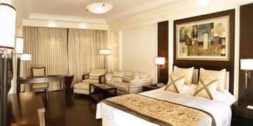 Quarto de hotel com uma cama grande, uma escrivaninha, uma cadeira, um sofá e um quadro na parede.