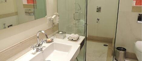 A modern bathroom with a large mirror, two sinks, a glass shower enclosure, and a toilet.