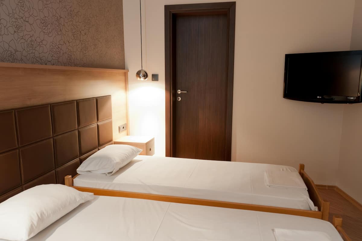 Habitación de hotel con dos camas individuales, cabecero de madera, televisor de pantalla plana montado en la pared y una puerta con manija.