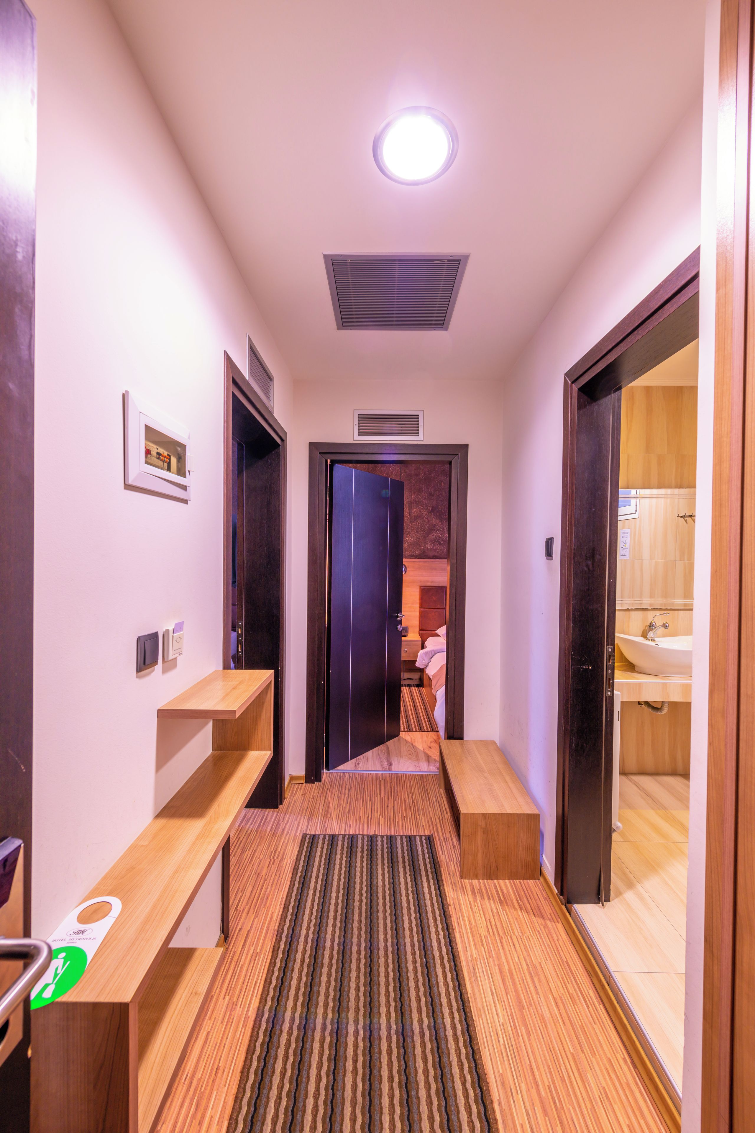Passadís d'hotel amb una boscaterra de fusta, una catifa amb dibuixos i una porta que dona a un bany.