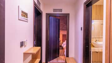 Un pasillo de hotel con un banco de madera, alfombra estampada y una puerta que da a un baño.