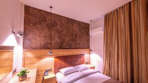 A modern hotel room with a wooden headboard, a bedside table with a lamp, a small plant, and a neatly made bed. - Metropolis (Serres)