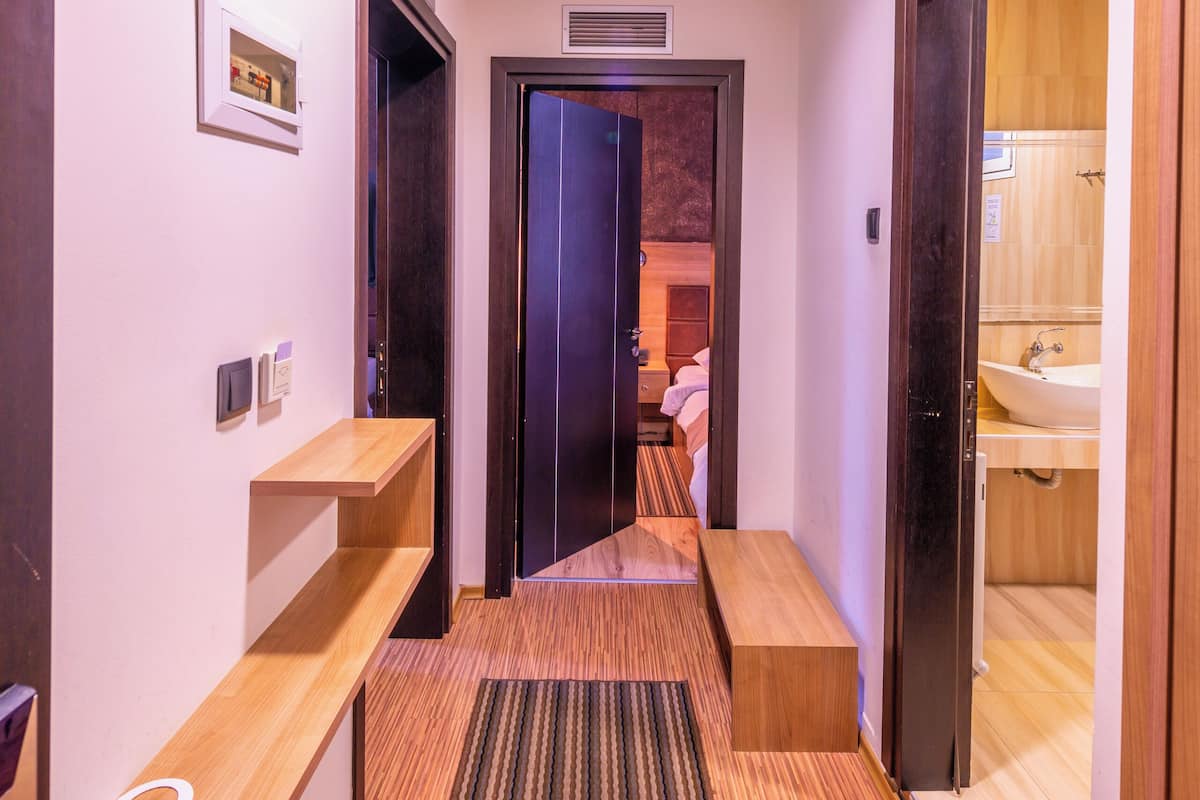 Un pasillo con un banco de madera, un tapete texturizado, una puerta que da al baño y una lámpara en el techo.