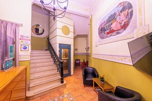 Un vestíbulo con una escalera, una recepción, un área de descanso y un mural en la pared.