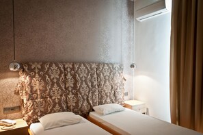 Habitación de hotel con una cama grande, una mesita de noche y un aire acondicionado de pared. Tiene una ventana con cortinas.