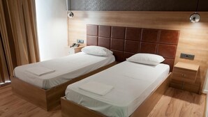 A hotel room with two wooden beds, a nightstand, and a small drawer unit. - Metropolis (Serres)