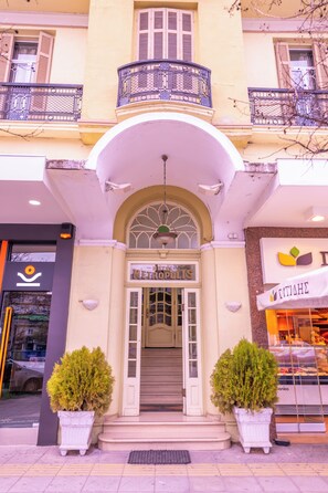 A hotel entrance with a double door, a balcony with a metal railing, and potted plants on either side. - Metropolis (Serres)
