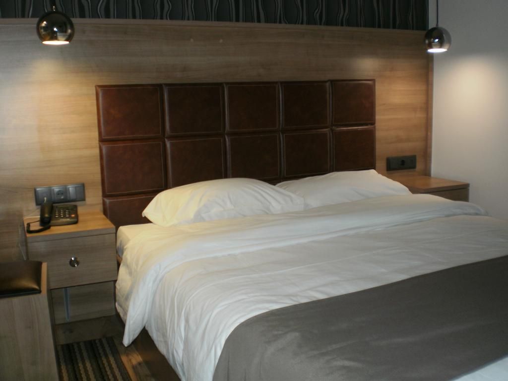 A hotel room with a wooden headboard, a single bed with white bedding, a bedside table with a lamp, and a telephone.