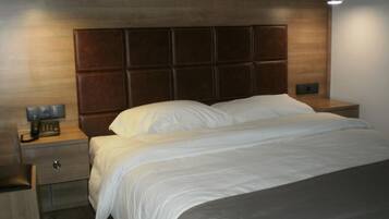 A hotel room with a wooden headboard, a single bed with white bedding, a bedside table with a lamp, and a telephone.