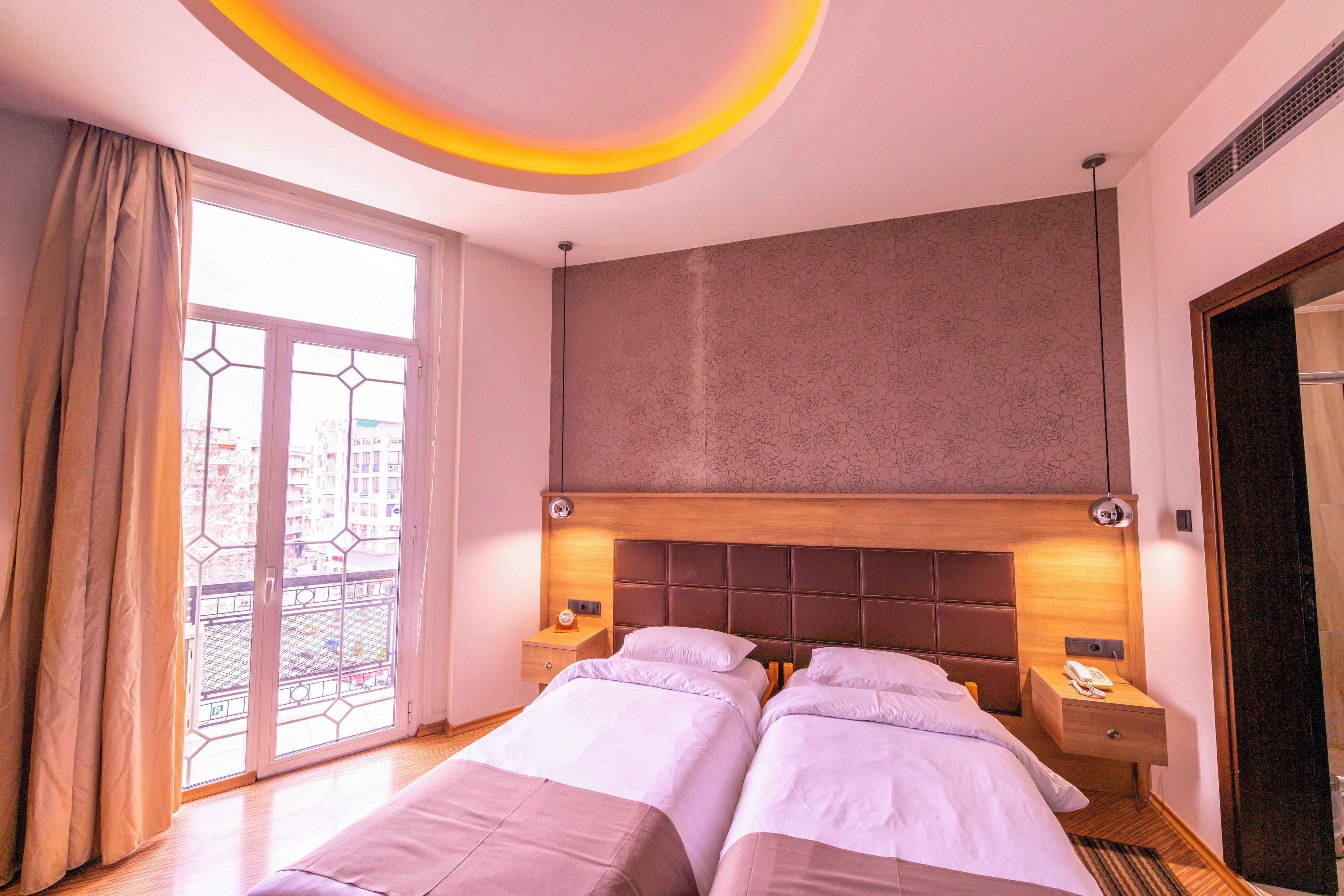 Ett hotellrum med två sängar, ett stort fönster med utsikt och en modern takdesign.