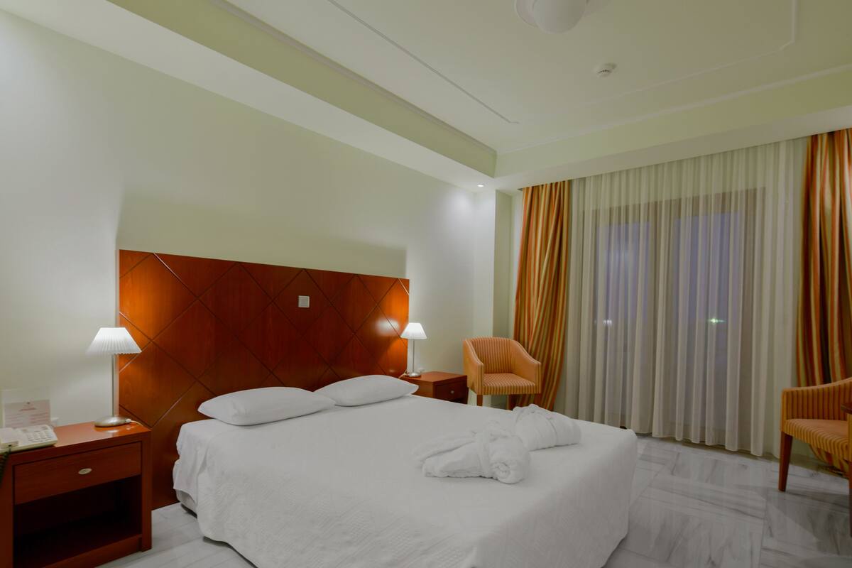 A hotel room with a large bed, two bedside tables, a chair, and a window with curtains.