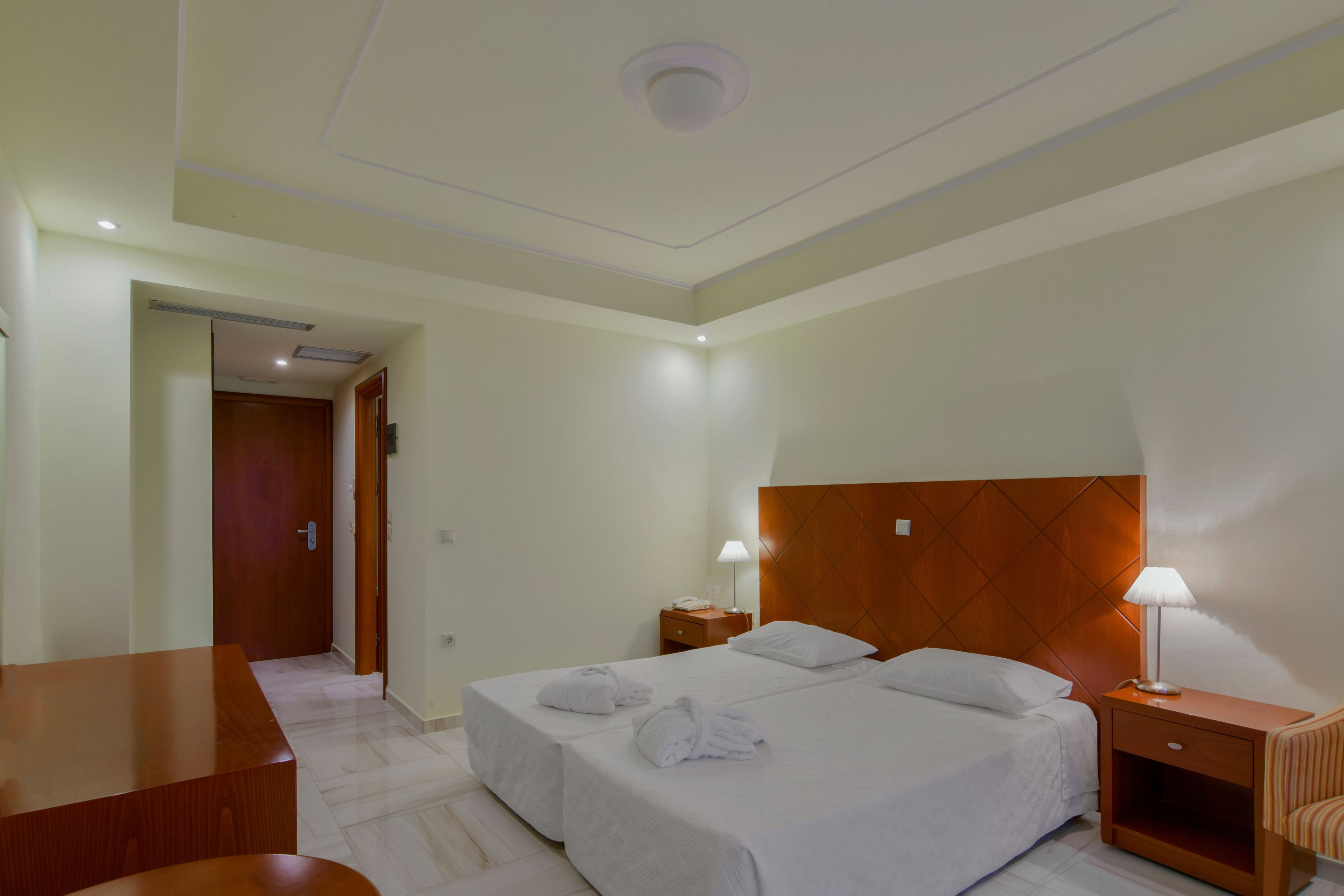 A hotel room with a large bed, two bedside tables, a wooden headboard, and a desk with a chair.
