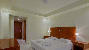 A hotel room with a large bed, two bedside tables, a wooden headboard, and a desk with a chair.