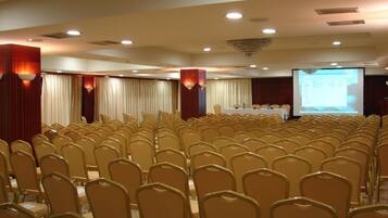 A conference room with rows of chairs, a projection screen, and a table with microphones.