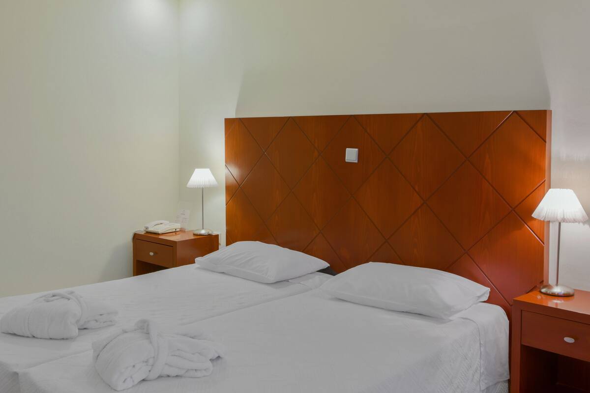 A hotel room with a large bed, two bedside tables, a wooden headboard, and white bedding.