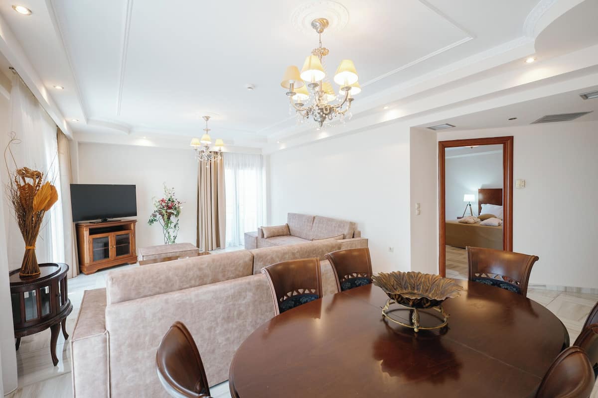 A modern living room with a large round dining table, beige sofas, and a chandelier.
