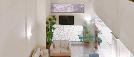 Amplia sala de estar con techo alto, televisor de pantalla plana montado en la pared y una disposición de sofás y mesa de centro.
