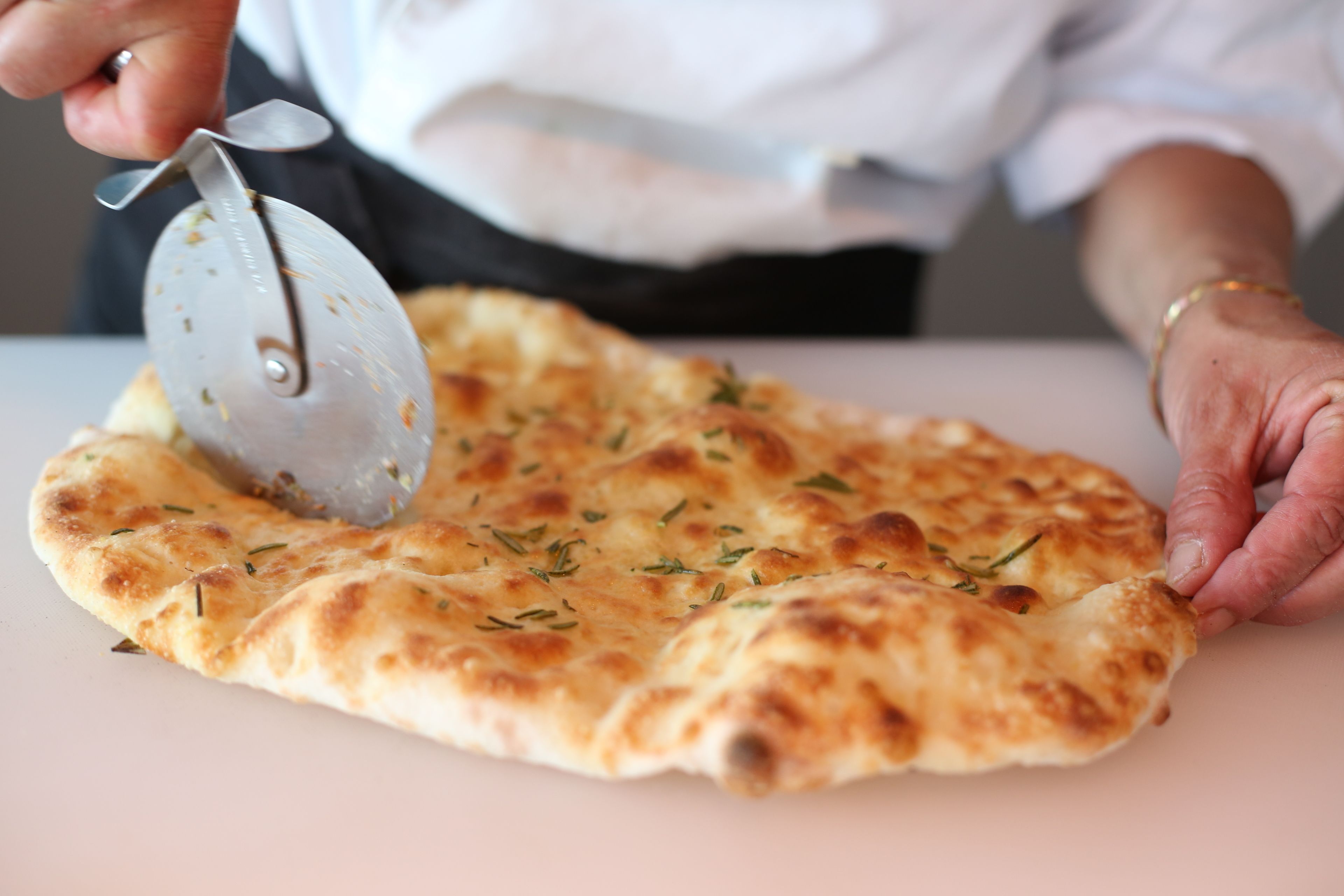 A person cutting a flatbread with a pizza cutter.
