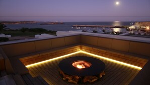 Eine Dachterrasse mit Feuerstelle mit Blick auf einen Yachthafen und die Küste.
